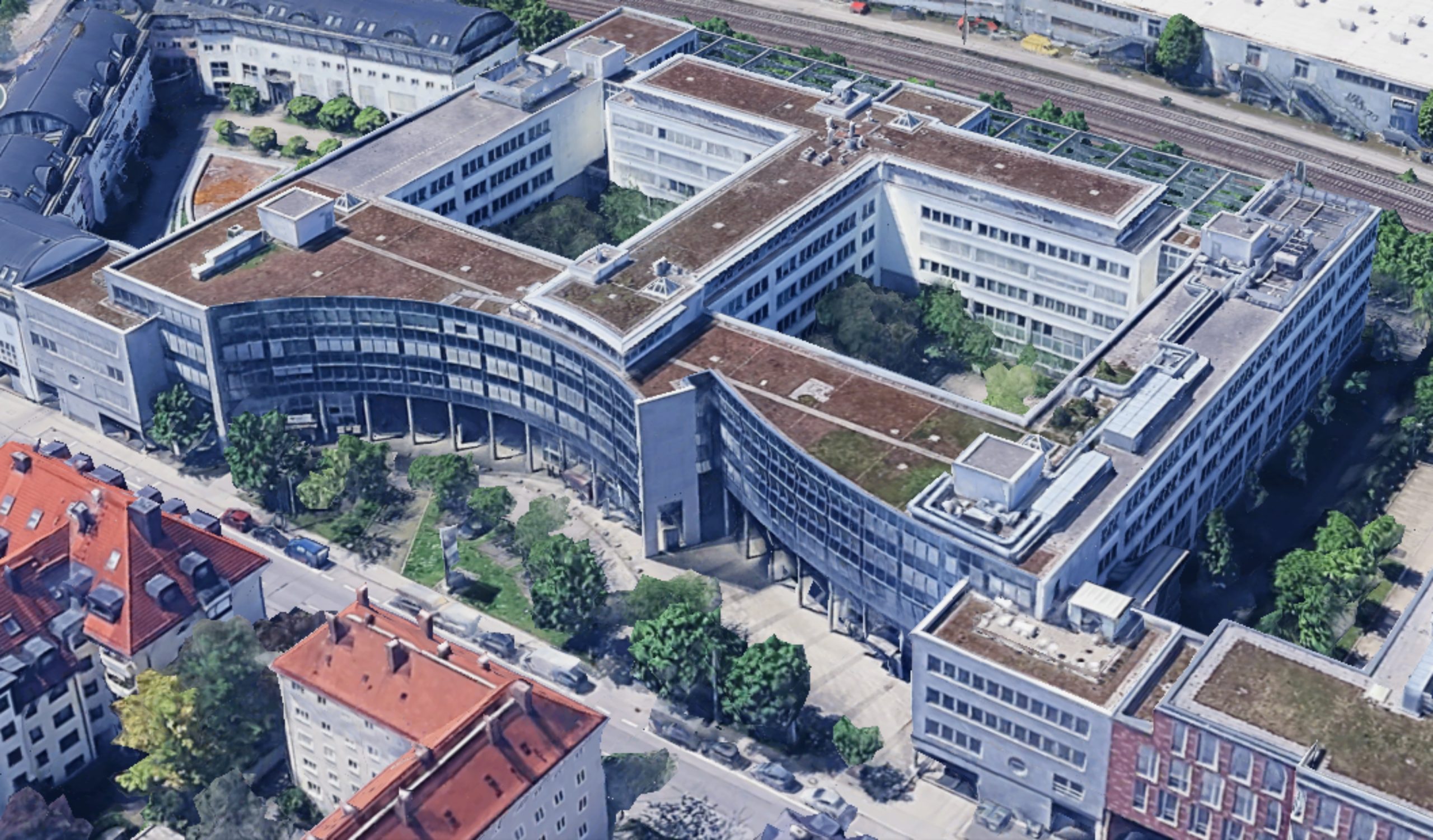 Luftaufnahme eines modernen Büro- und Verwaltungsgebäudekomplexes mit begrünten Flachdächern in städtischer Lage nahe einer Bahntrasse