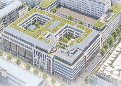 Schrägansicht eines großen, U‑förmigen Gebäudeblocks mit begrünten Dachflächen in dicht bebauter Innenstadtlage.