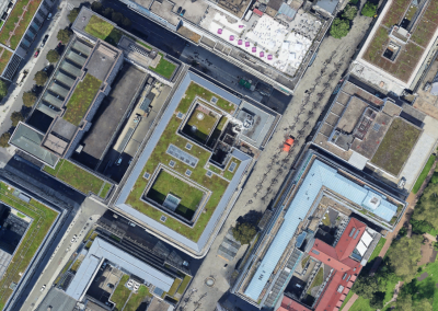 Luftbild eines großen Gebäudeblocks mit begrünten Dachflächen und umliegender Innenstadtbebauung.